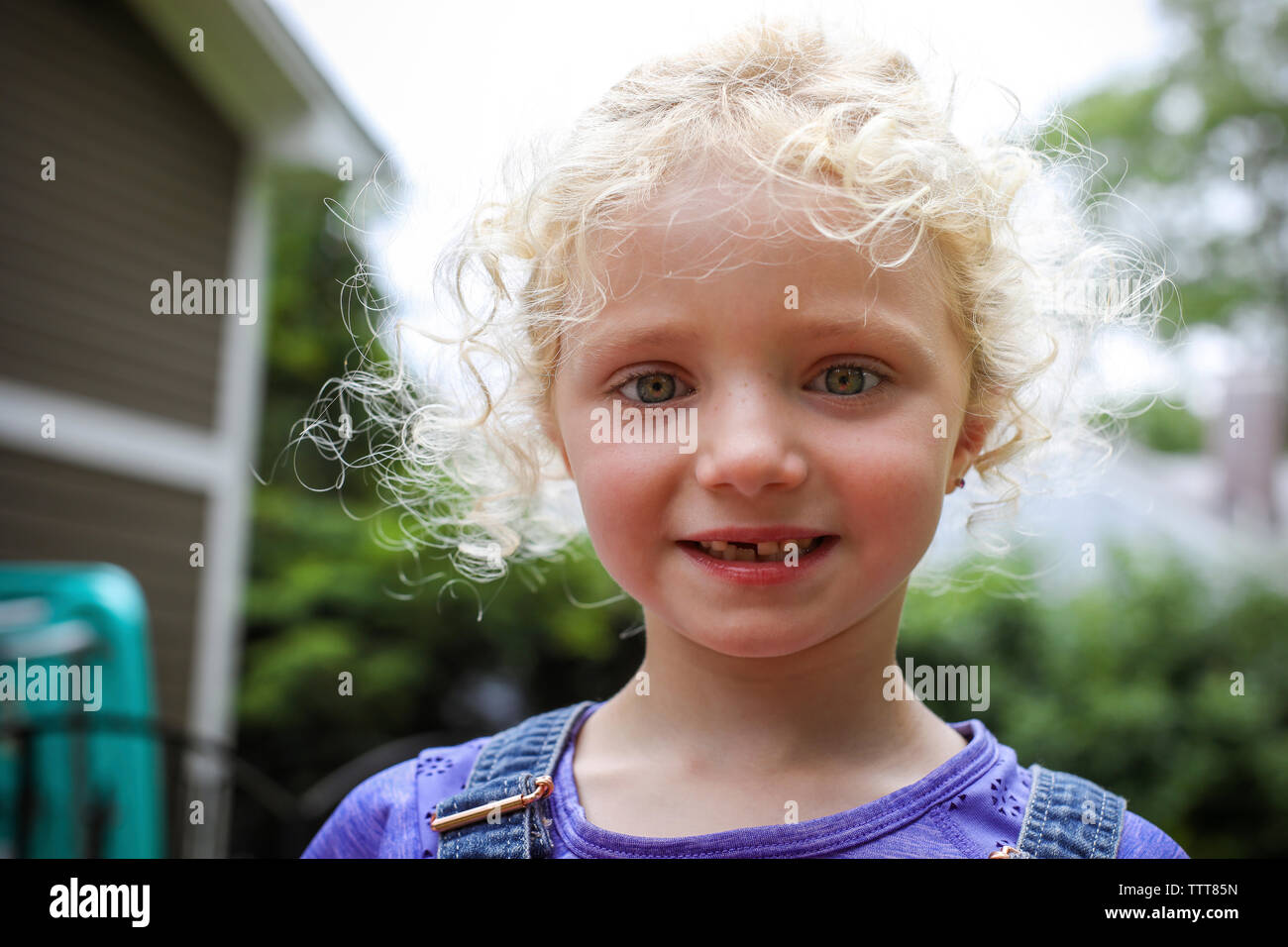 Close-up portrait of cute fille avec des cheveux blonds en désordre à la cour contre le ciel permanent Banque D'Images