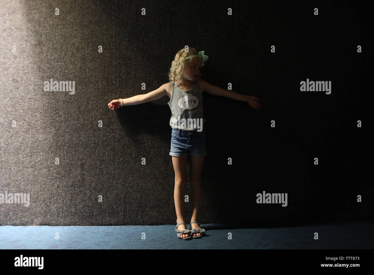 Petite fille dans l'ombre contre le mur sombre en short Banque D'Images