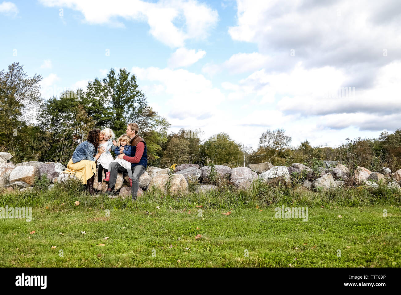 Famille de quatre assis sur un mur de pierre avec un ciel bleu au-dessus Banque D'Images