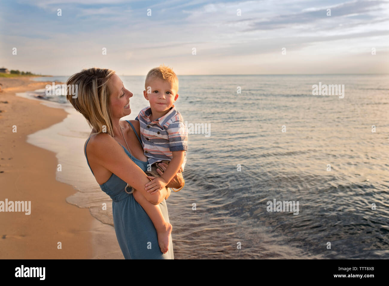 Portrait of cute fils porté par la mère à la plage pendant le coucher du soleil Banque D'Images
