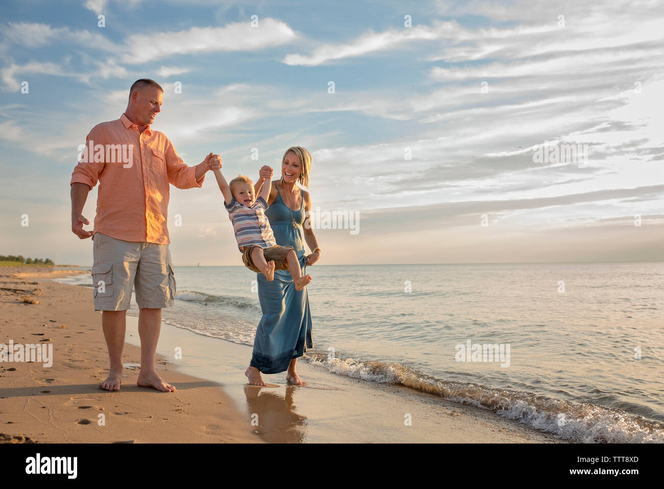 Les parents ludique holding fils mains tout en lui balançant at beach Banque D'Images