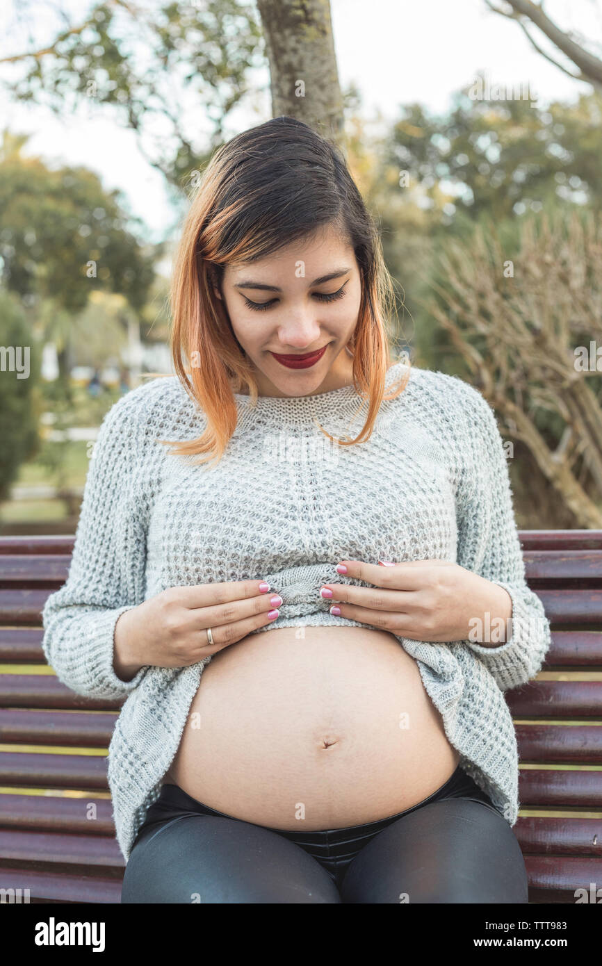 Portrait d'une jeune femme enceinte, montrant son ventre au parc Banque D'Images