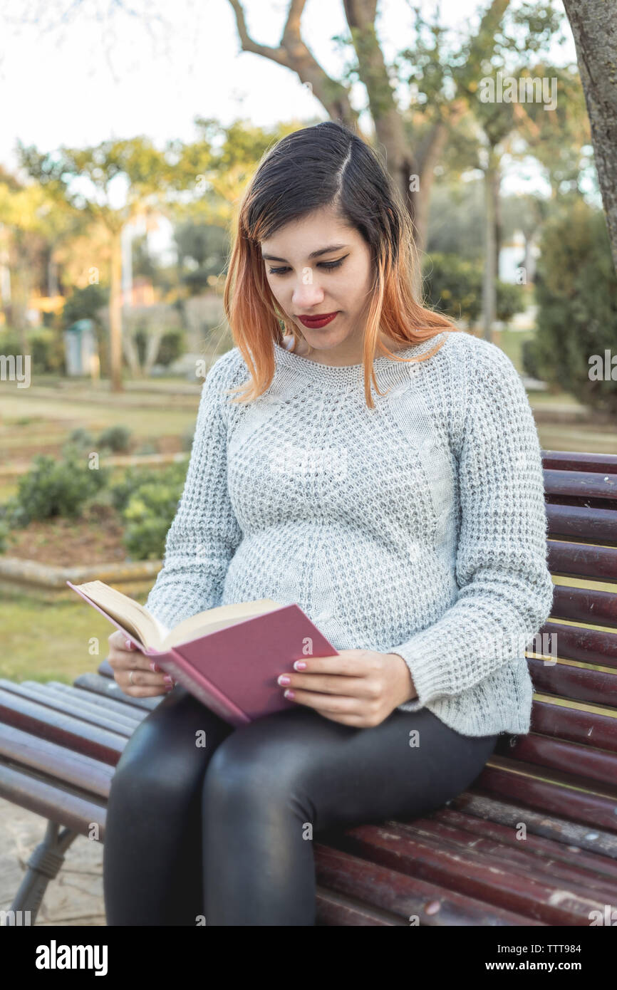 Portrait d'une jeune femme enceinte assis dans le parc et la lecture Banque D'Images