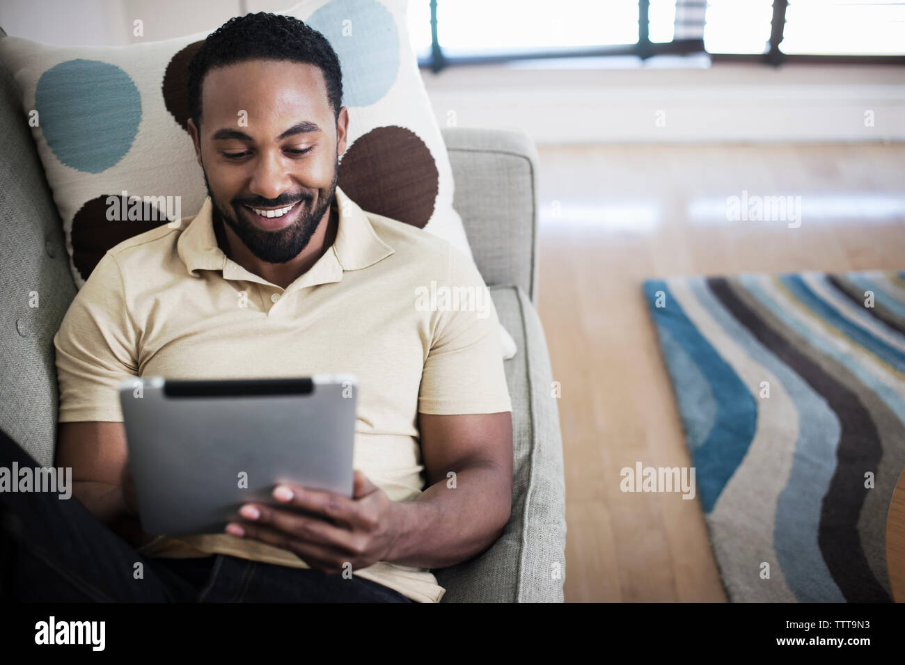 Smiling man using tablet while sitting on sofa at home Banque D'Images