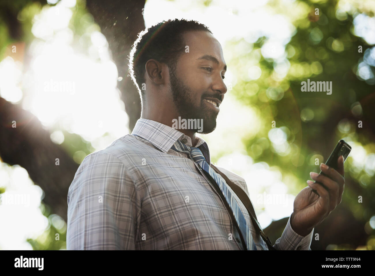 Smiling man holding phone en se tenant sur le sunny day Banque D'Images