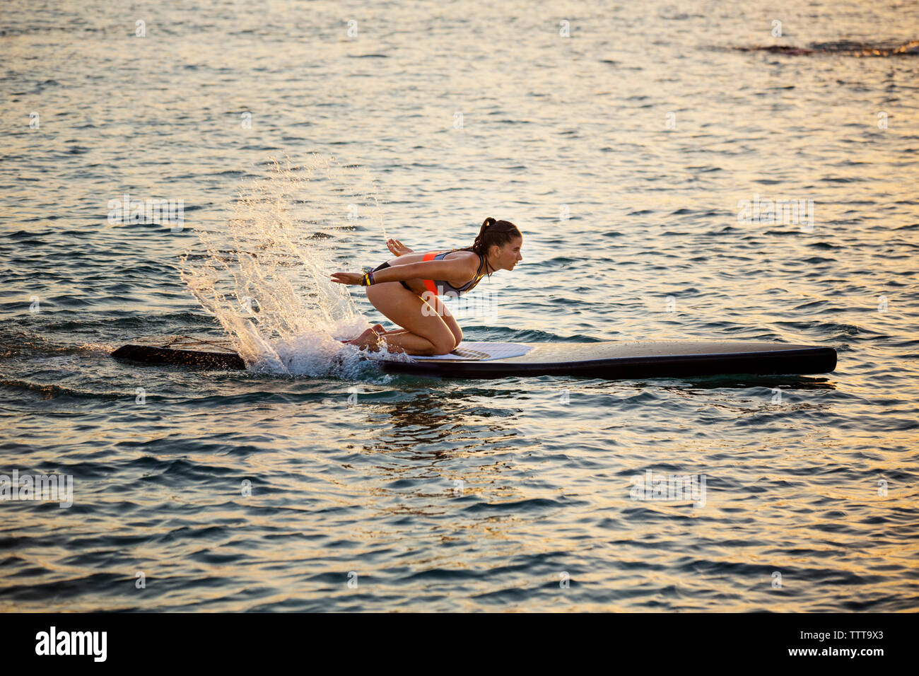 Femme agenouillée sur le paddleboard tandis que les projections d'eau de mer Banque D'Images