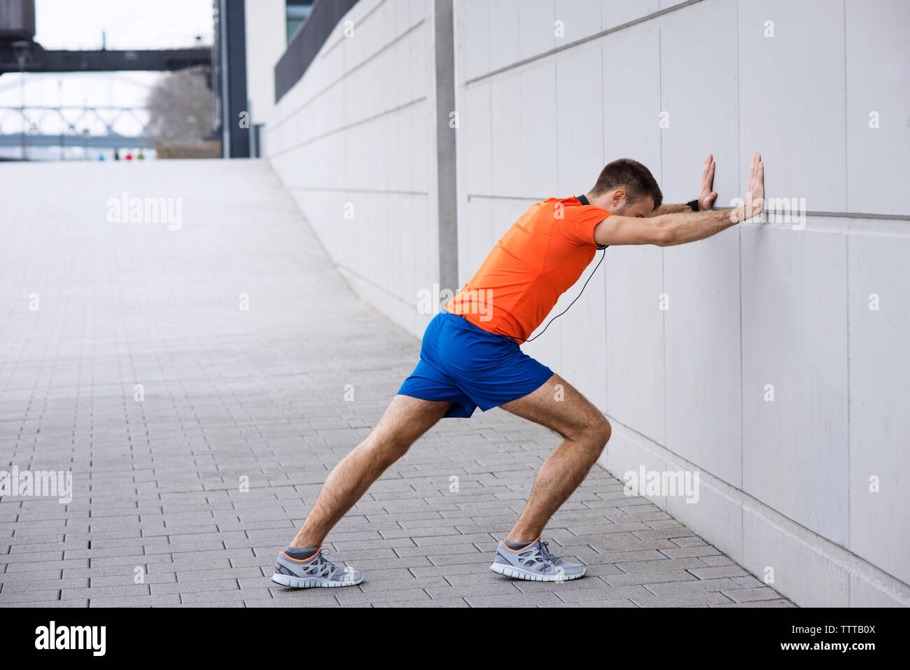Vue latérale de l'athlète masculin leaning on wall tout en exerçant sur sentier Banque D'Images