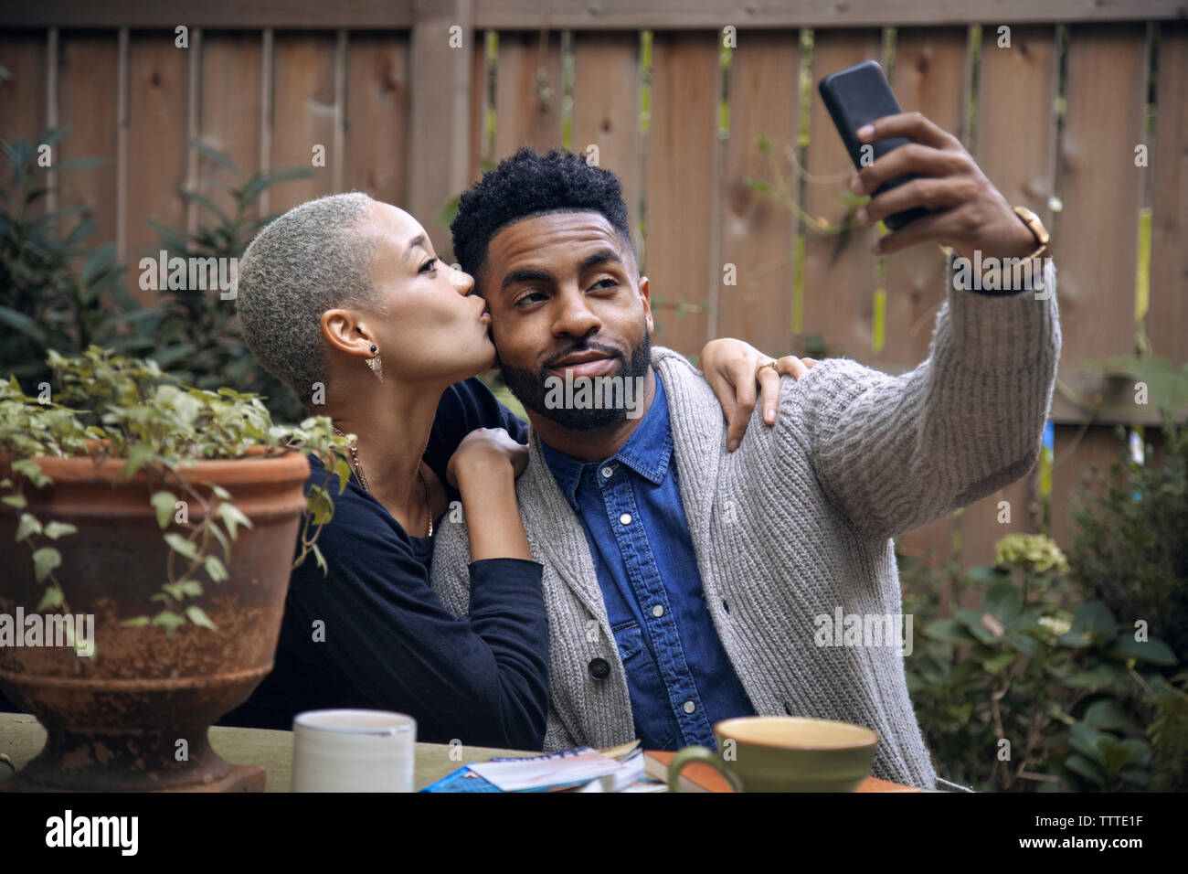 Woman kissing boyfriend tout en tenant en arrière-cour selfies Banque D'Images