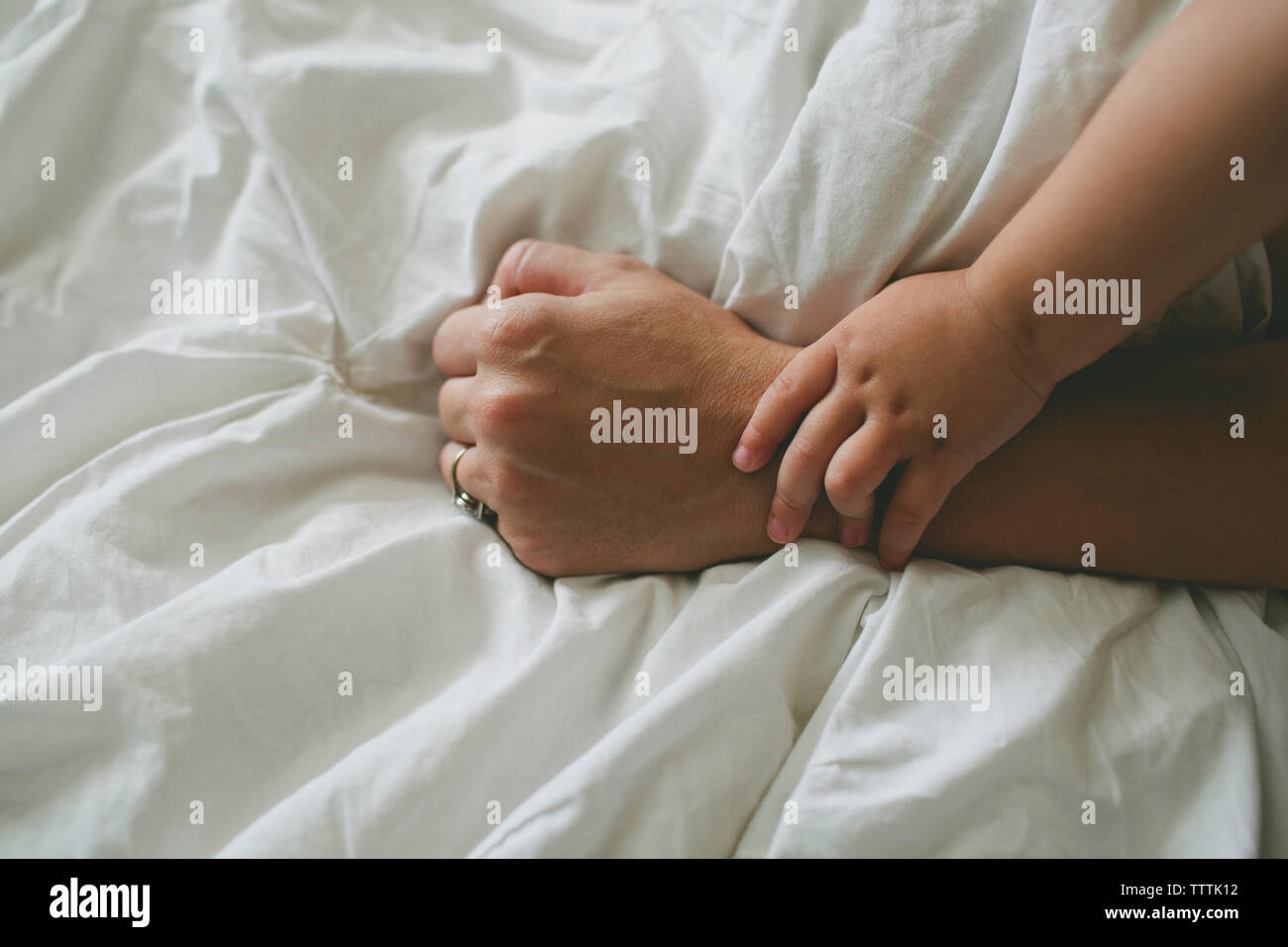 Portrait of boy holding mother's hand on bed Banque D'Images