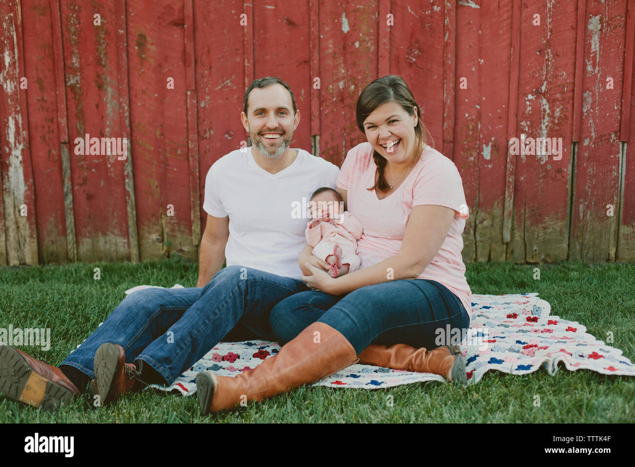 Portrait of happy mother and father with baby girl sitting on field in yard Banque D'Images