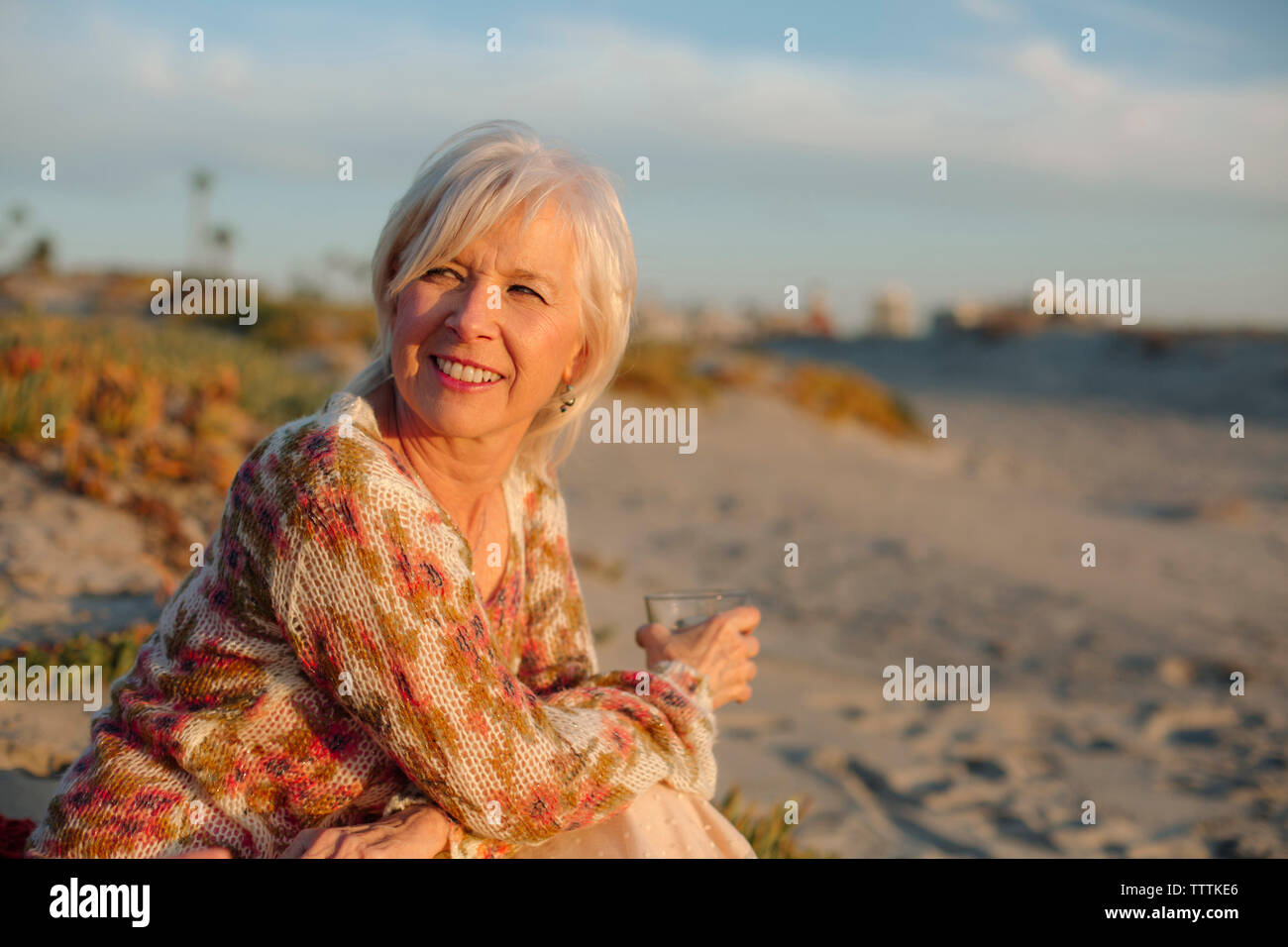 Une femme à boire assis à la plage pendant le coucher du soleil Banque D'Images