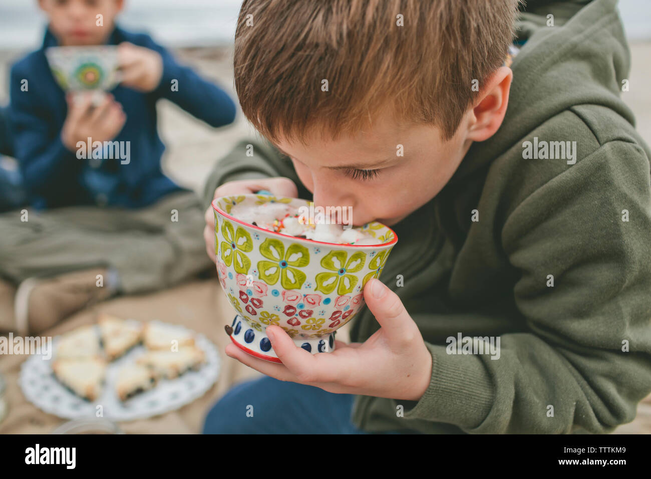 Boy drinking from cup alors qu'il était assis à la plage avec son frère en arrière-plan Banque D'Images