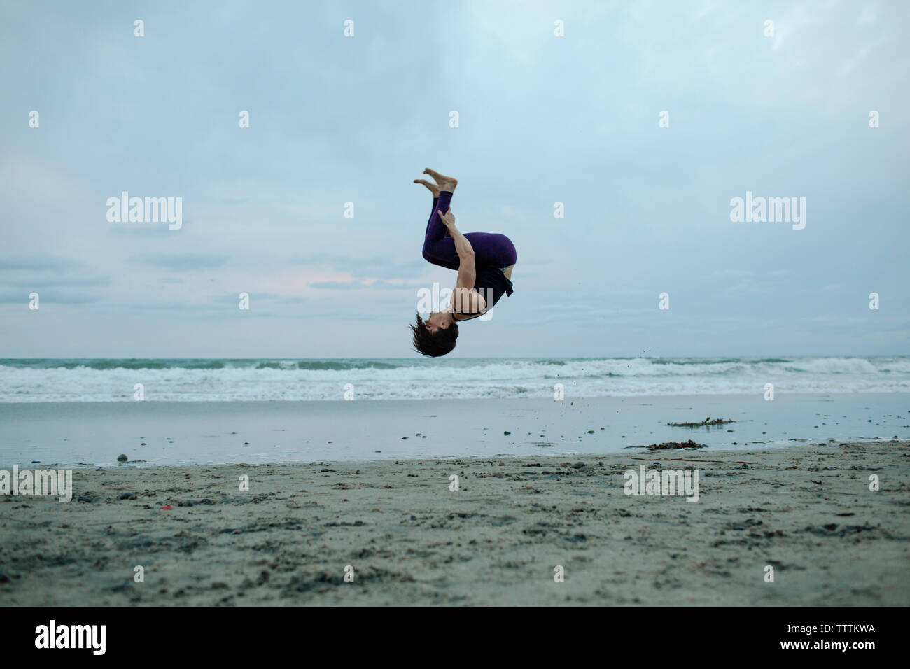 Femme insouciante à backflipping beach tout en s'exerçant contre le ciel Banque D'Images