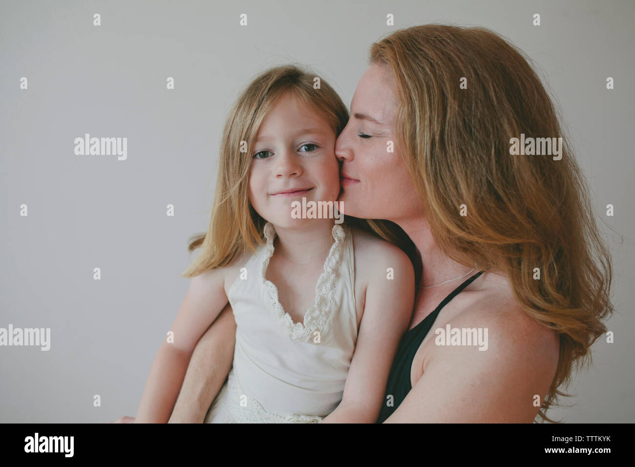 Portrait of fille avec la mère de l'embrasser contre fond blanc Banque D'Images