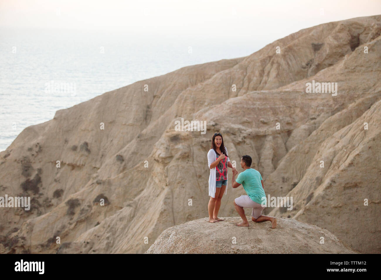 Petit ami de proposer le mariage à petite amie en s'agenouillant sur la roche contre la mer Banque D'Images