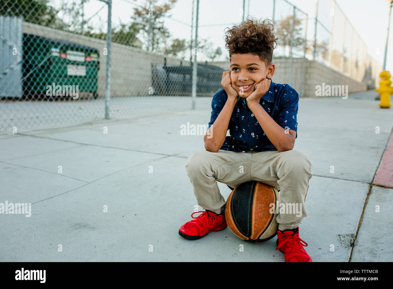 Garçon assis sur une balle sur un terrain de basket-ball Banque D'Images