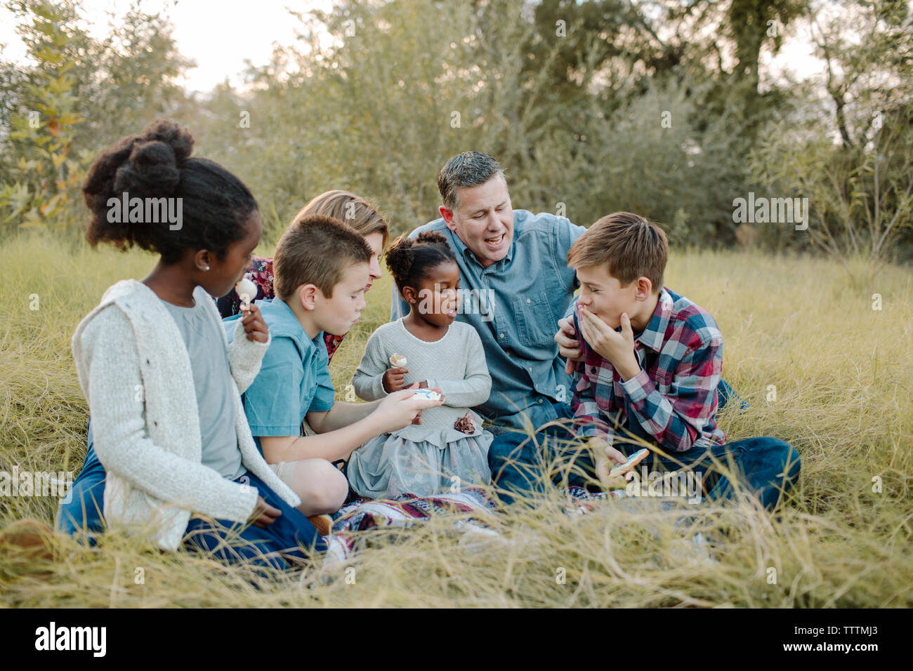 Les parents des enfants ayant de la nourriture tout en restant assis sur le champ à park Banque D'Images