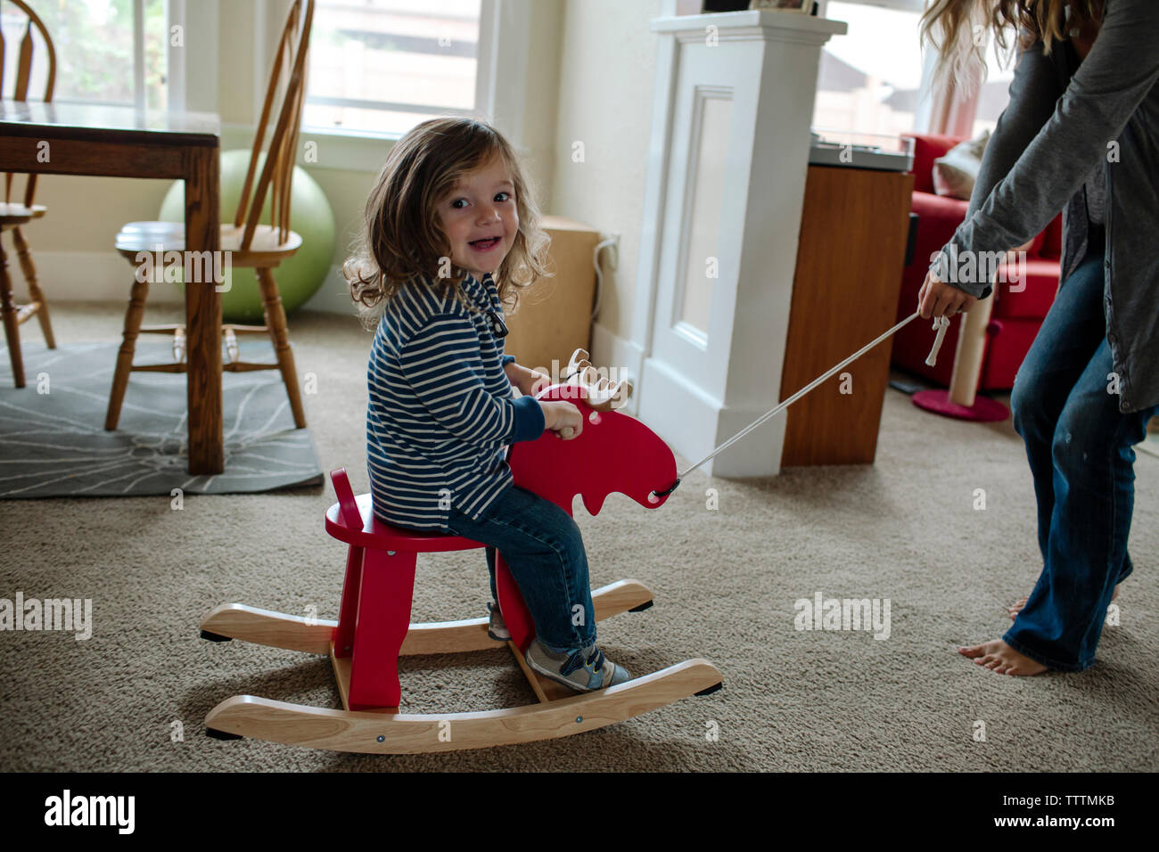 Portrait of cheerful fille assise sur le renne bascule en jouant avec la mère à la maison Banque D'Images