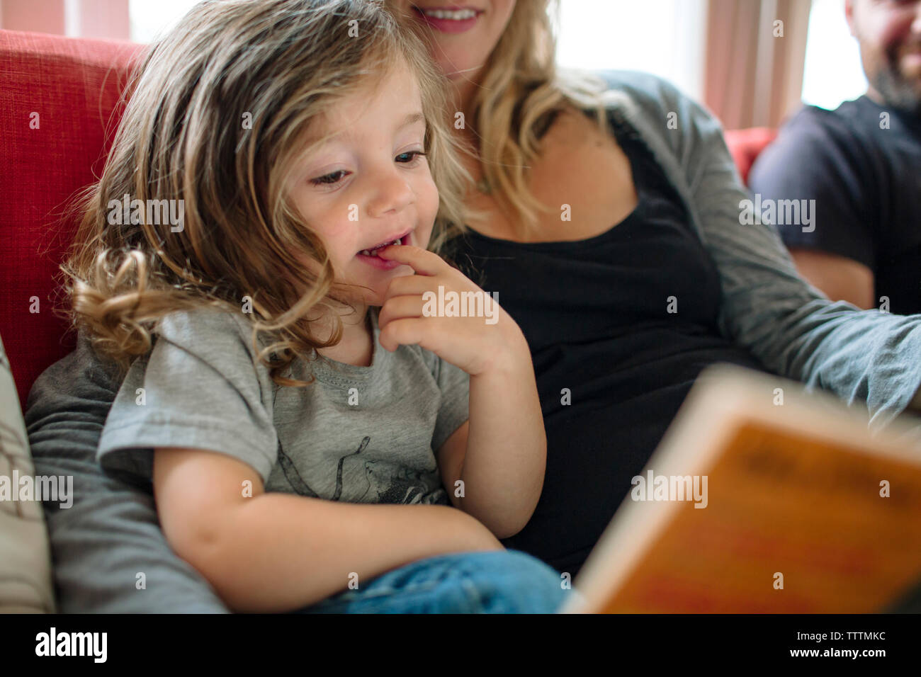 Fille mignonne avec le doigt dans la bouche à la recherche au Réservez en position assise par mère sur canapé à la maison Banque D'Images