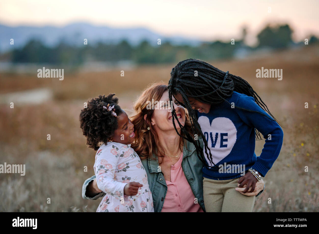 Smiling mother jouer avec les filles à la forêt durant le coucher du soleil Banque D'Images