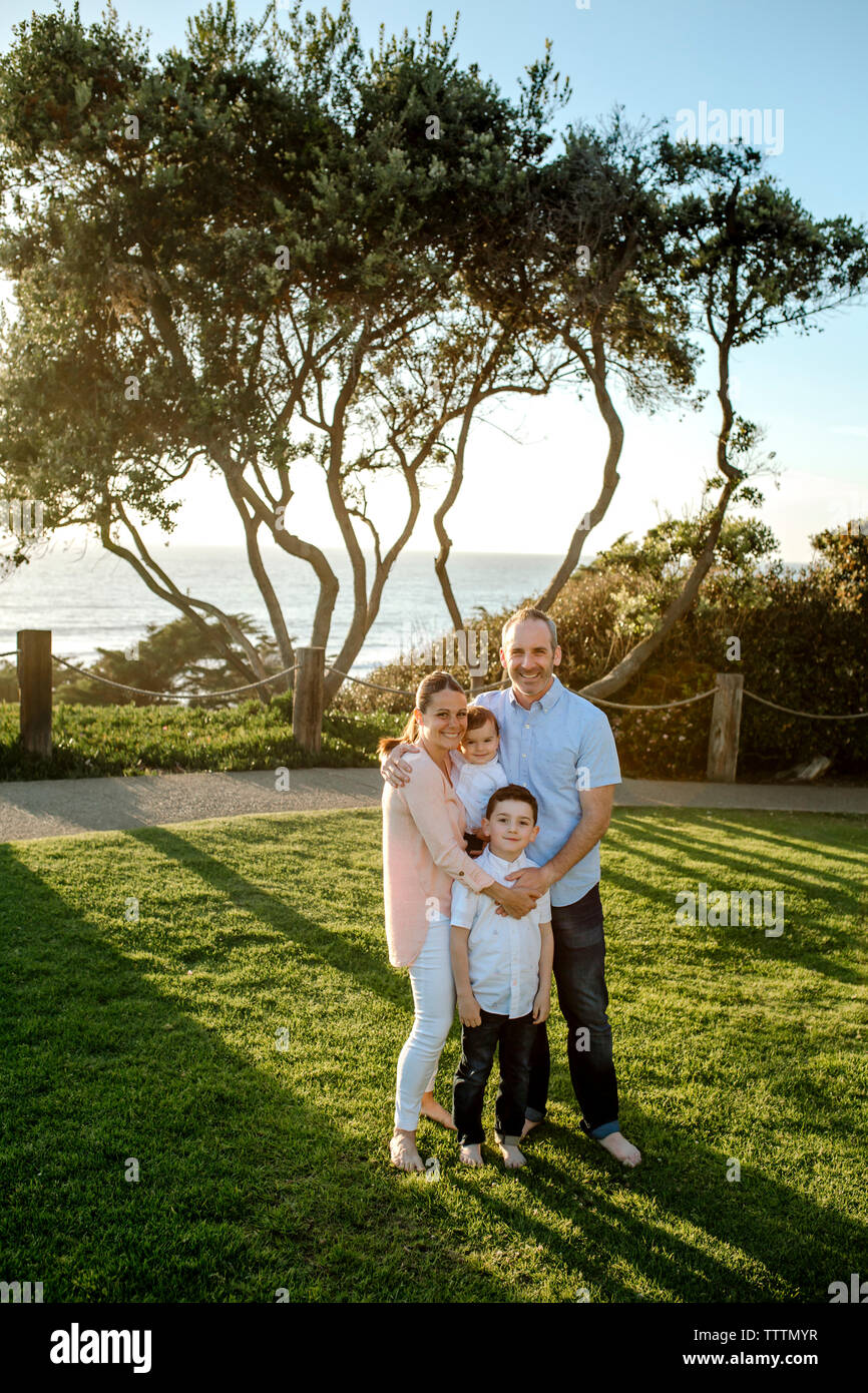 Portrait of happy family standing on grassy field par mer contre ciel clair Banque D'Images