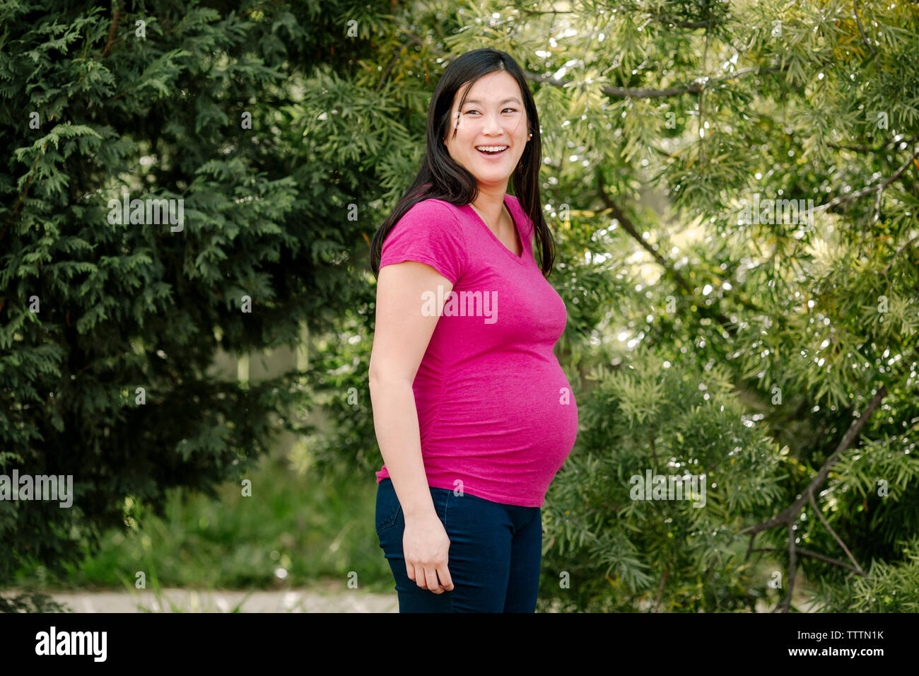 Cheerful pregnant woman debout contre des arbres au parc Banque D'Images