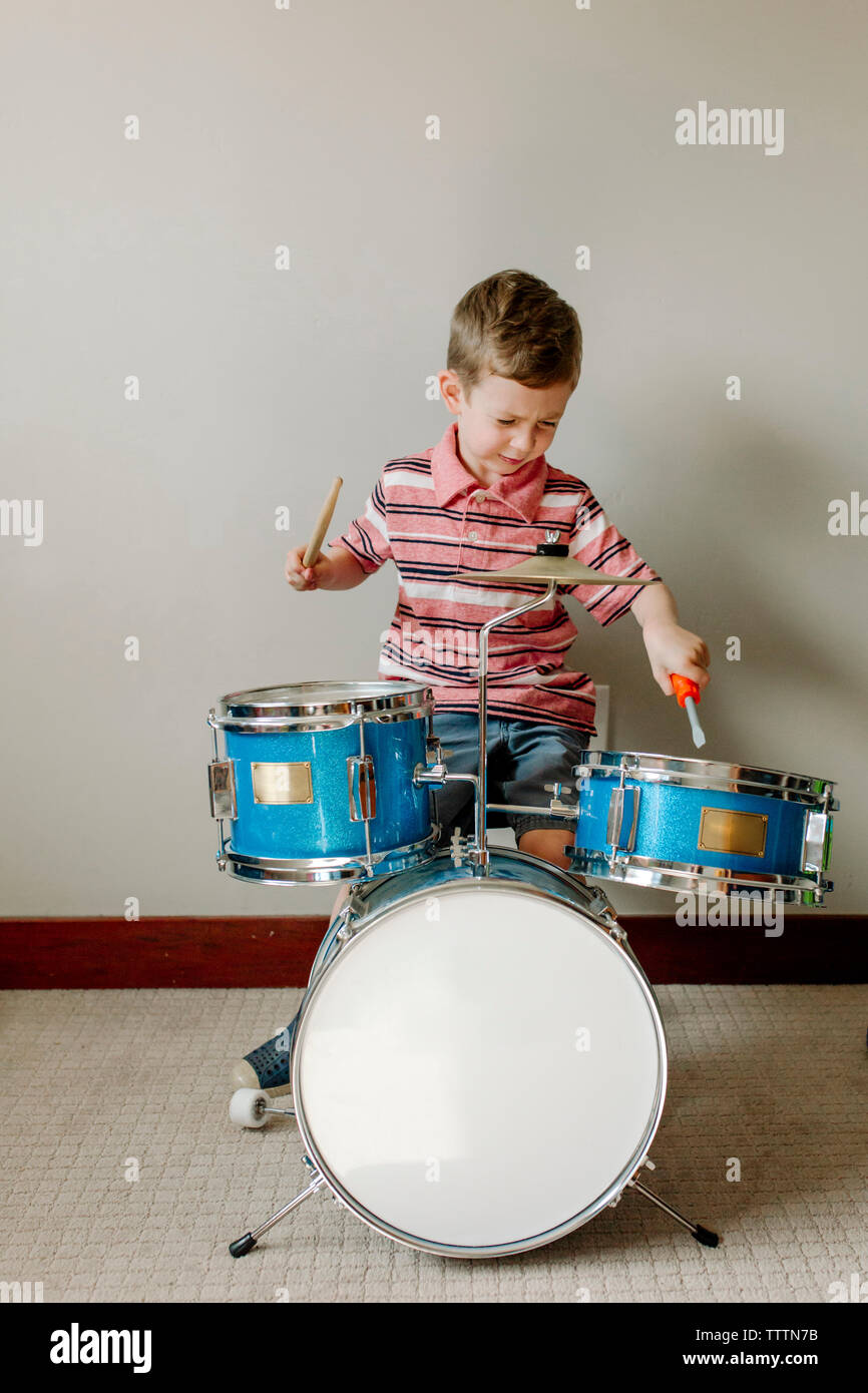 Cute boy à jouer de la batterie alors qu'il était assis contre le mur à la  maison Photo Stock - Alamy