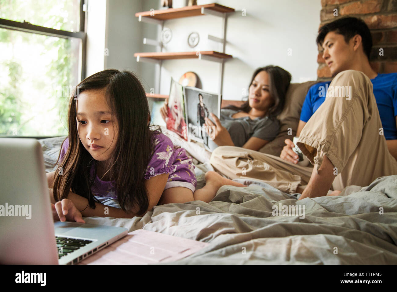 Fille à l'aide d'un ordinateur portable tout en étant assis avec les parents sur le lit chez lui Banque D'Images