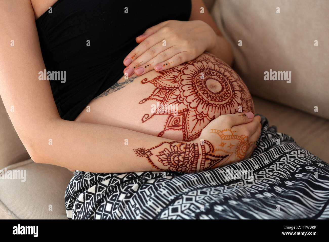 Jeune femme enceinte avec tatouage au henné sur le ventre, assis sur un  canapé dans la chambre Photo Stock - Alamy