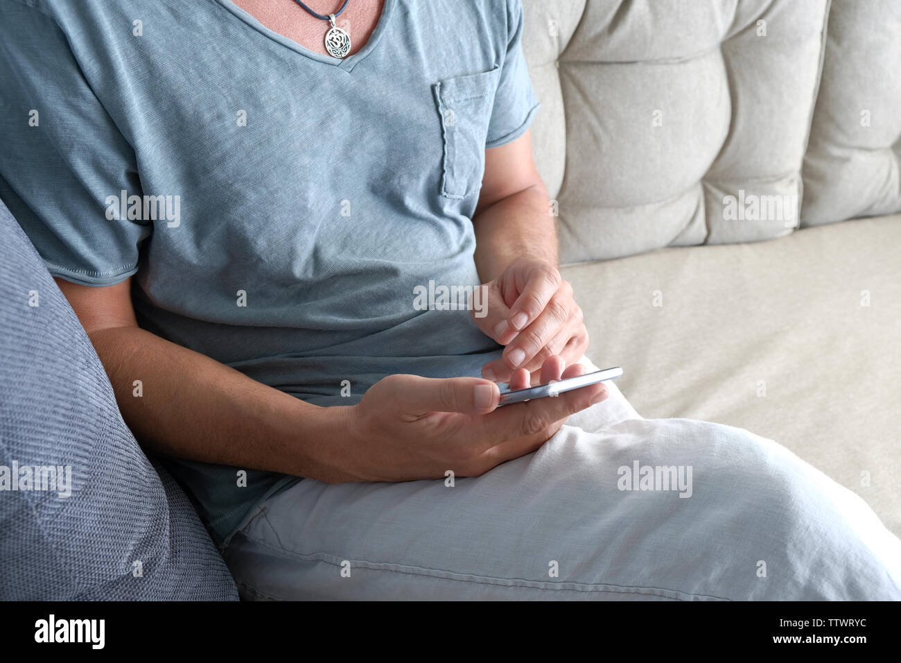L'homme dans des vêtements décontractés assis sur un canapé à la maison un message SMS sur son mobilephone Banque D'Images