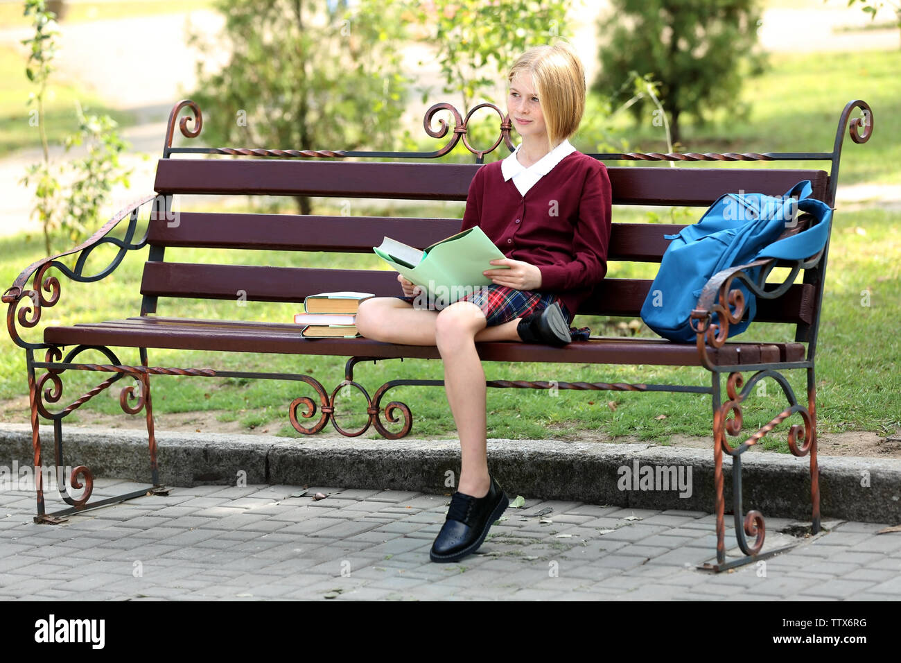 Lycéenne reading book while sitting on bench in park Banque D'Images