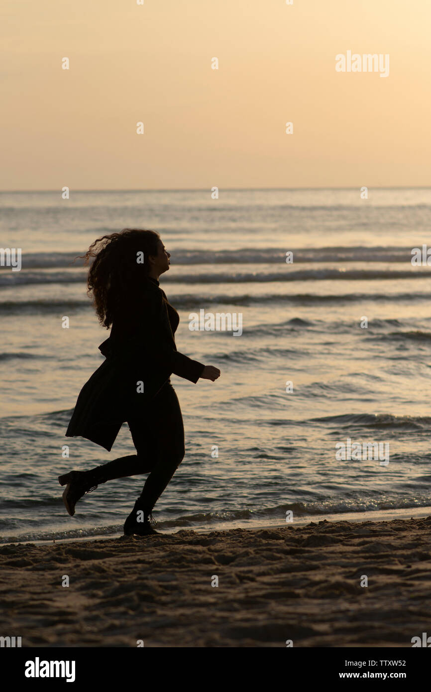 Manteau femme portant d'exécution sur la plage au coucher du soleil Banque D'Images