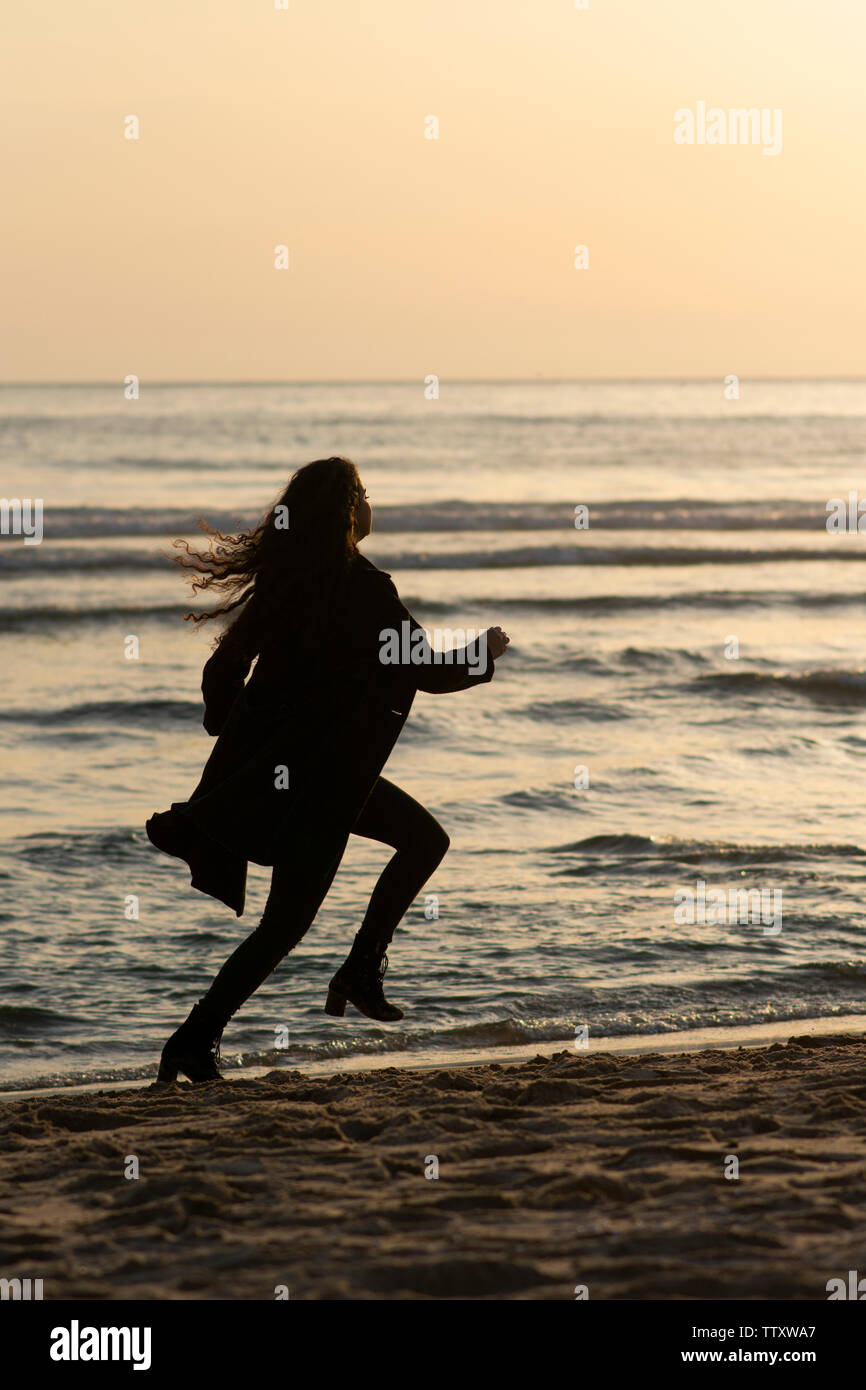 Manteau femme portant d'exécution sur la plage au coucher du soleil Banque D'Images