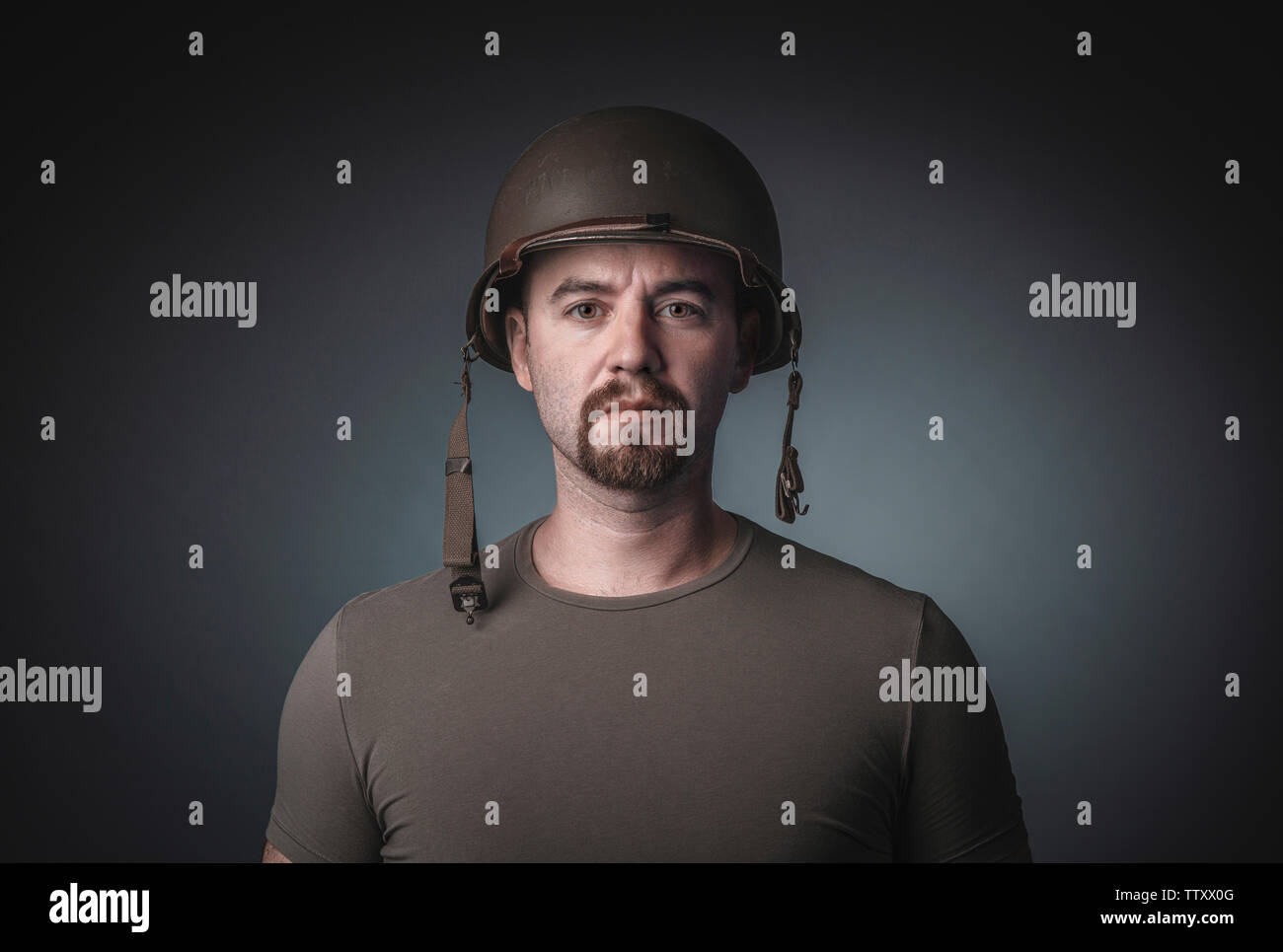 Portrait d'un homme dans un t-shirt portant un casque militaire du soldat, fixant la caméra. Banque D'Images