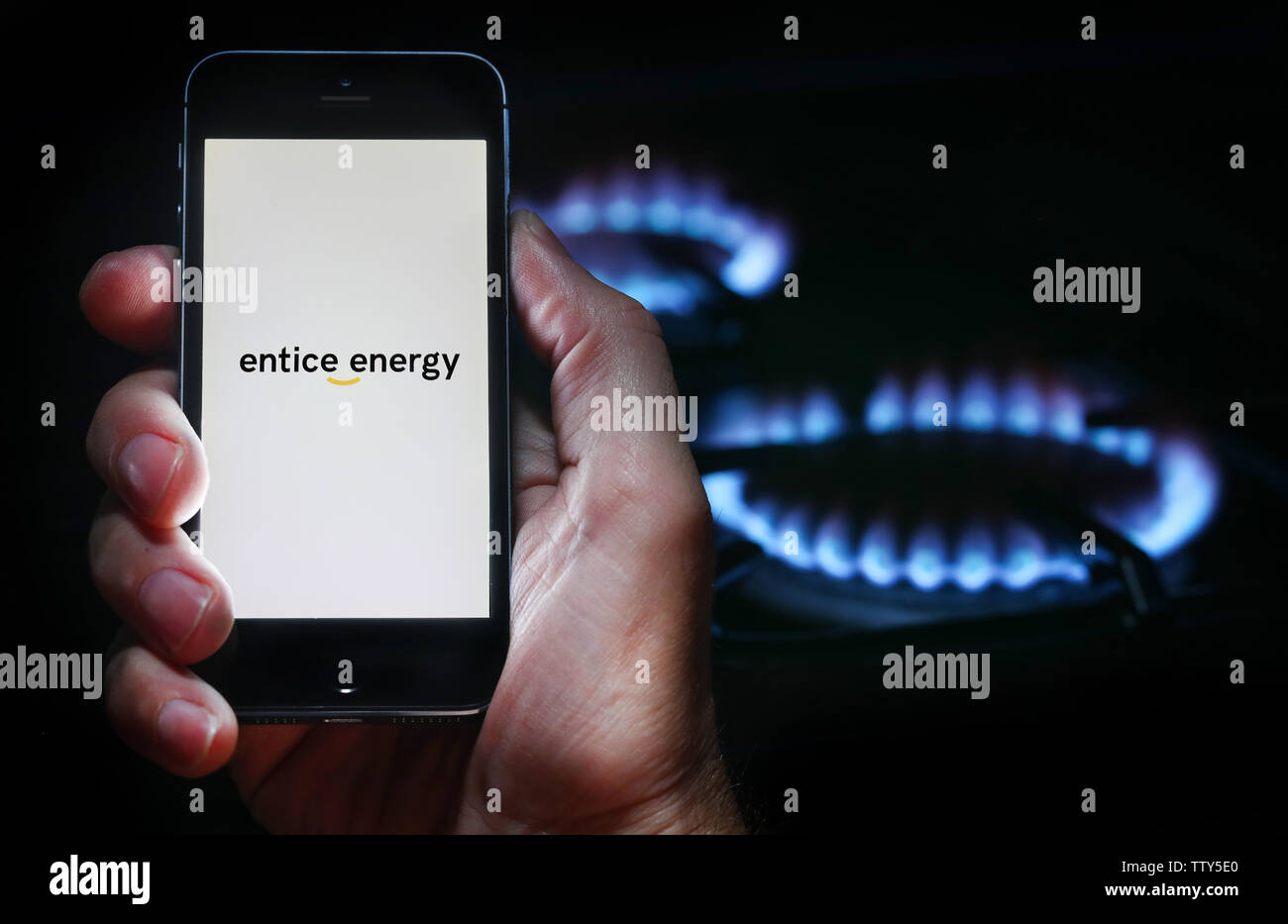 Un homme à la recherche sur le site web logo pour inciter l'entreprise Énergie Énergie sur son téléphone devant sa cuisinière à gaz (usage éditorial uniquement) Banque D'Images