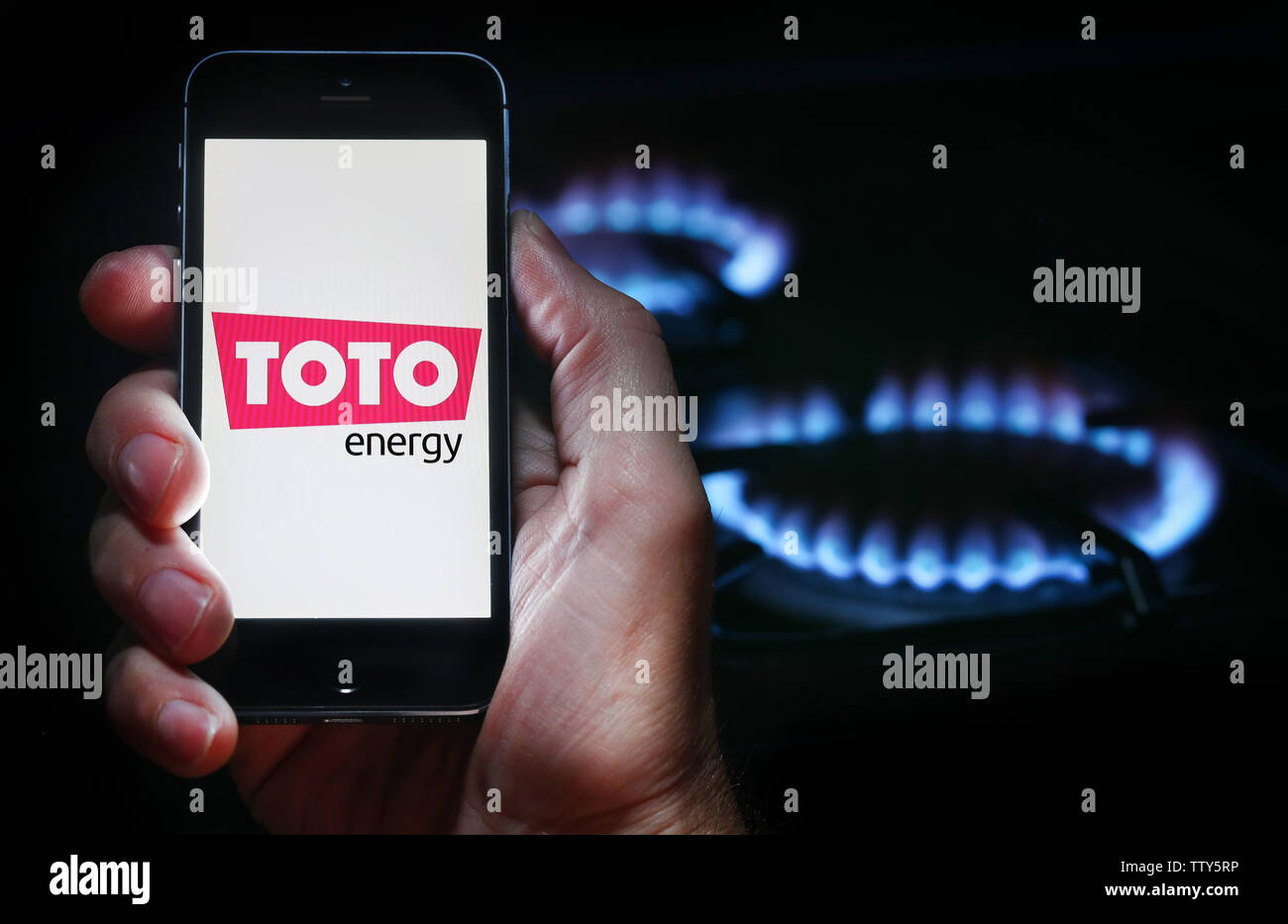 Un homme à la recherche sur le site web logo pour société de l'énergie Énergie Toto sur son téléphone devant sa cuisinière à gaz (usage éditorial uniquement) Banque D'Images