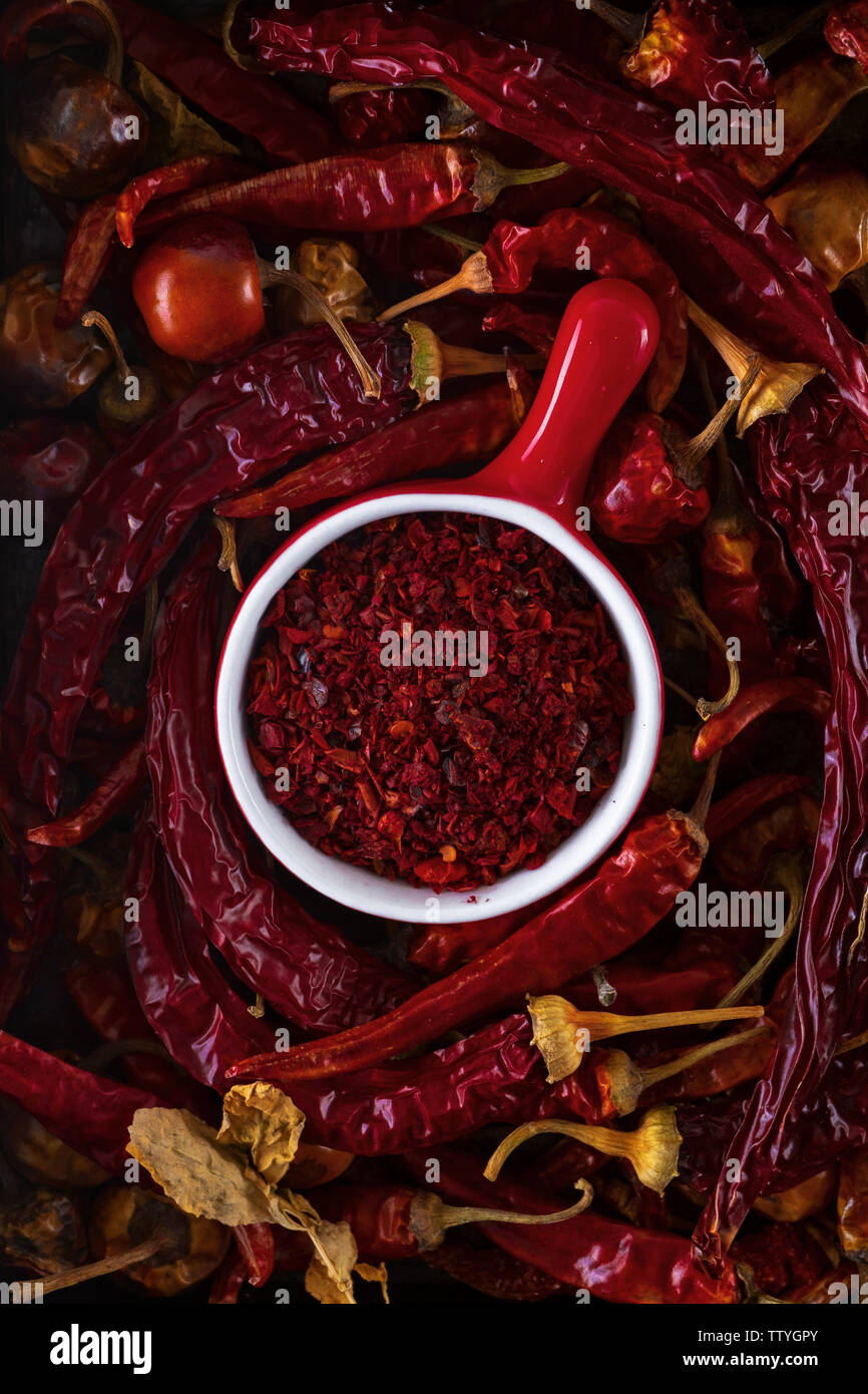 Tasse rouge avec rouge moulu entouré de gousses sèches de poivron rouge, vue de dessus, gros plan Banque D'Images