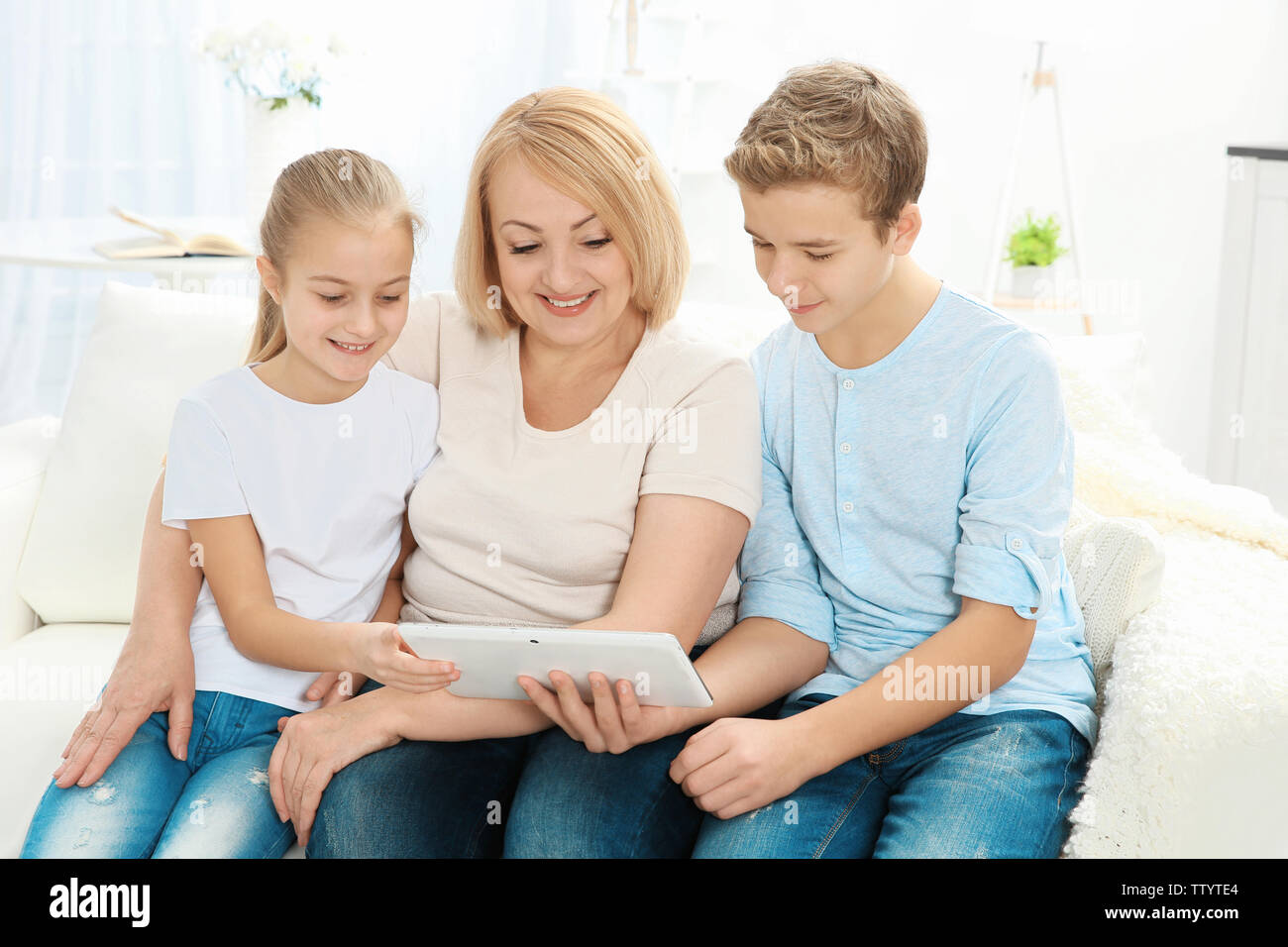 Mignon les enfants et leur grand-mère sitting on sofa with tablet computer Banque D'Images