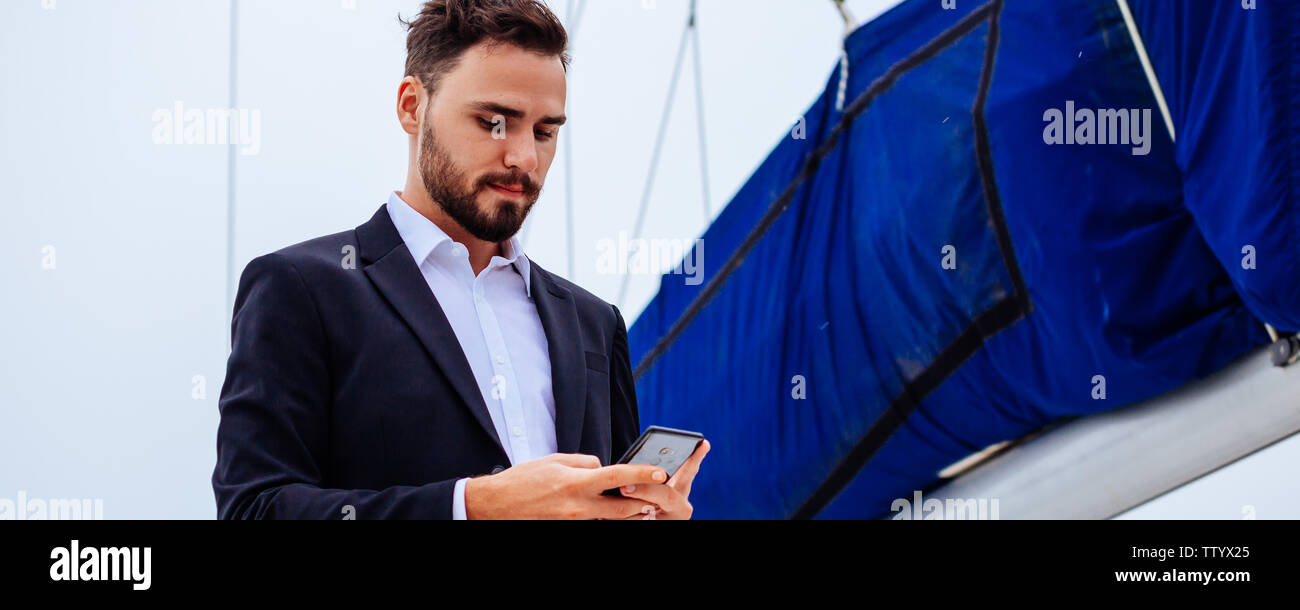 Les jeunes hommes d'beau using mobile phone on yacht de luxe en plein jour Banque D'Images