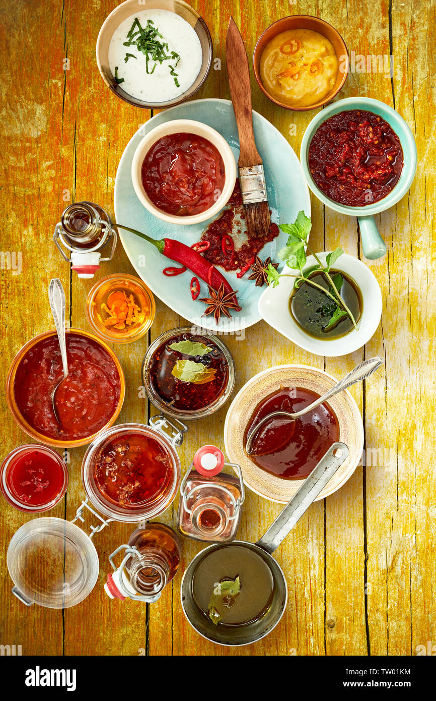 Sauces et Epices rouge vif avec des cuillères et divers ingrédients de fines herbes sur le dessus sur fond de bois brun rustique Banque D'Images