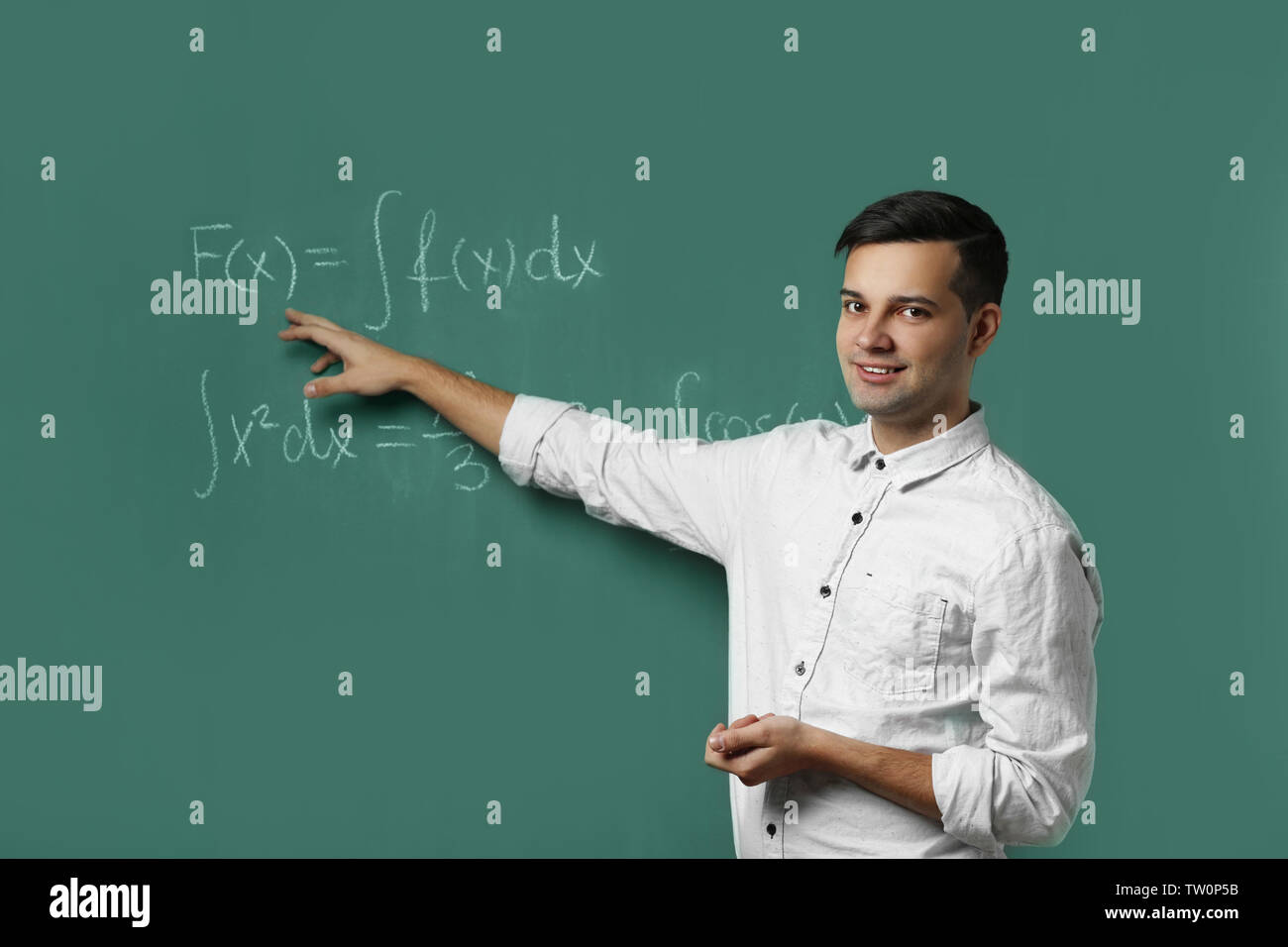 Beau jeune enseignant expliquant des formules mathématiques written on blackboard Banque D'Images