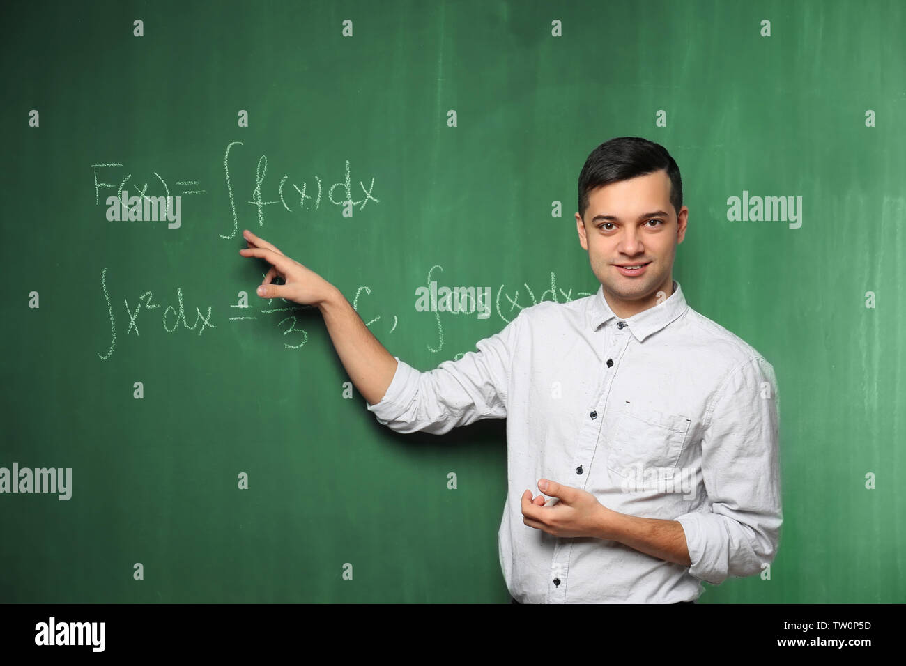 Beau jeune enseignant expliquant des formules mathématiques written on blackboard Banque D'Images