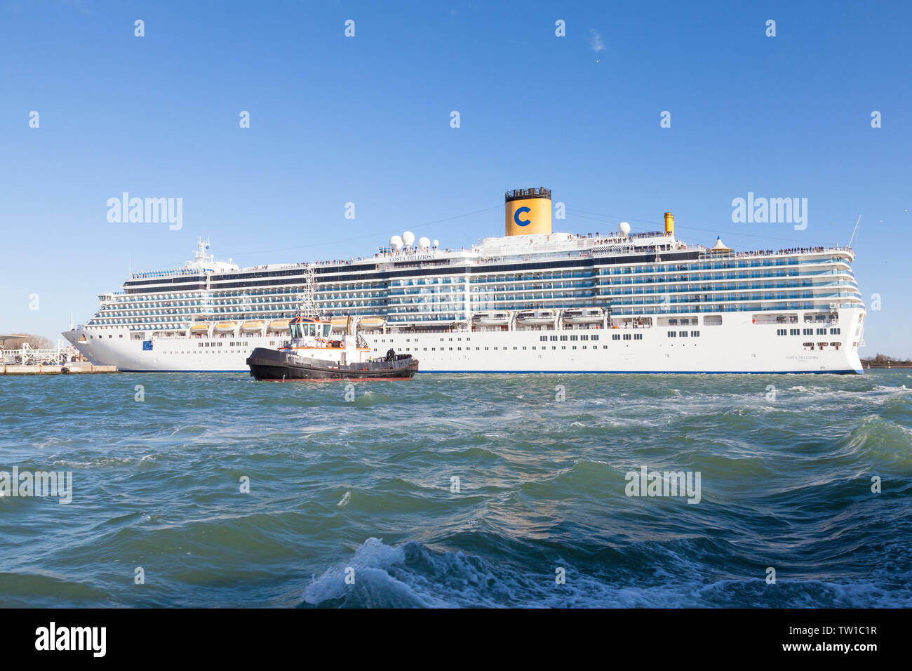 Paquebot de croisière passagers, le Costa Deliziosa, quitter le port en remorque par un remorqueur en mer agitée la sauvegarde dans le canal de la Giudecca, Venise, Vénétie, Italie Banque D'Images