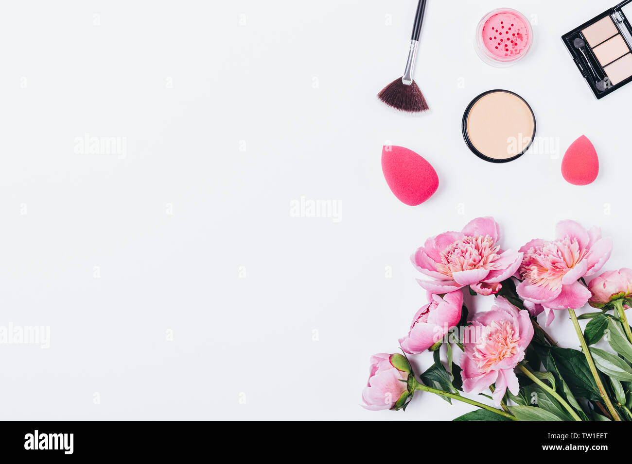 Arrière-plan de maquillage Poudre compacte avec brosse palette ombres à paupières, et d'éponges à côté de bouquet de fleurs de pivoine rose sur le tableau blanc, vue du dessus. Banque D'Images