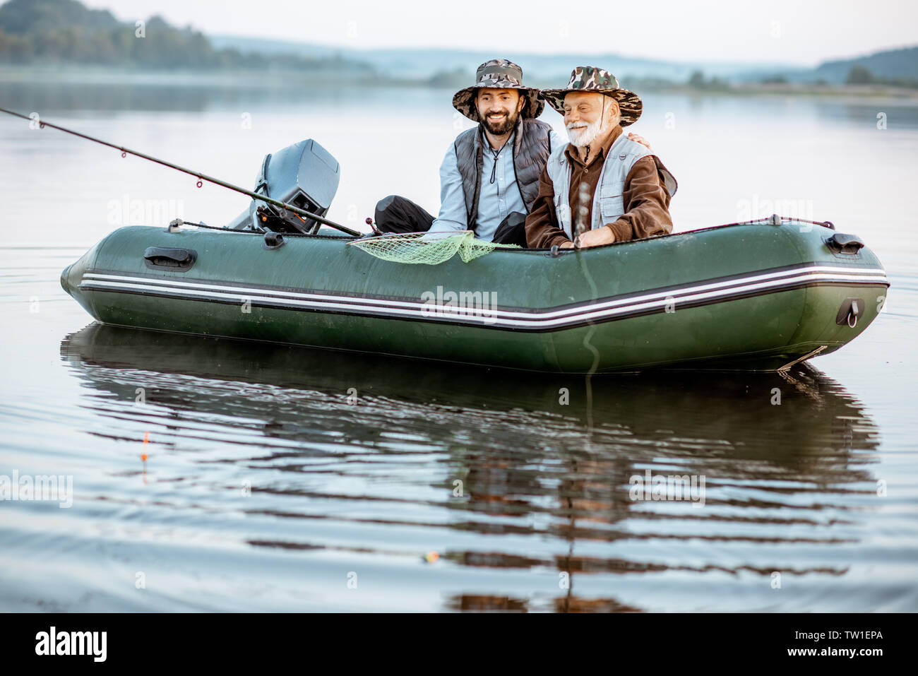 Portrait d'un grand-père avec des fils adultes de pêche sur le bateau gonflable sur le lac tôt le matin Banque D'Images