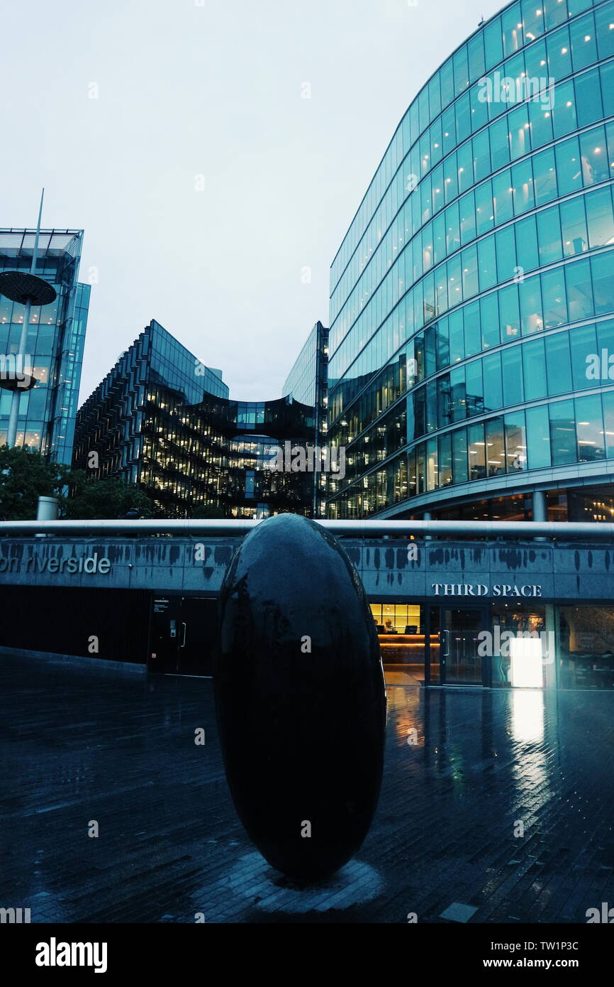 Le troisième espace de remise en forme dans la pluie et le soir et maisons en verre derrière elle à Londres, au Royaume-Uni. Dans l'avant-plan est une pierre. Banque D'Images