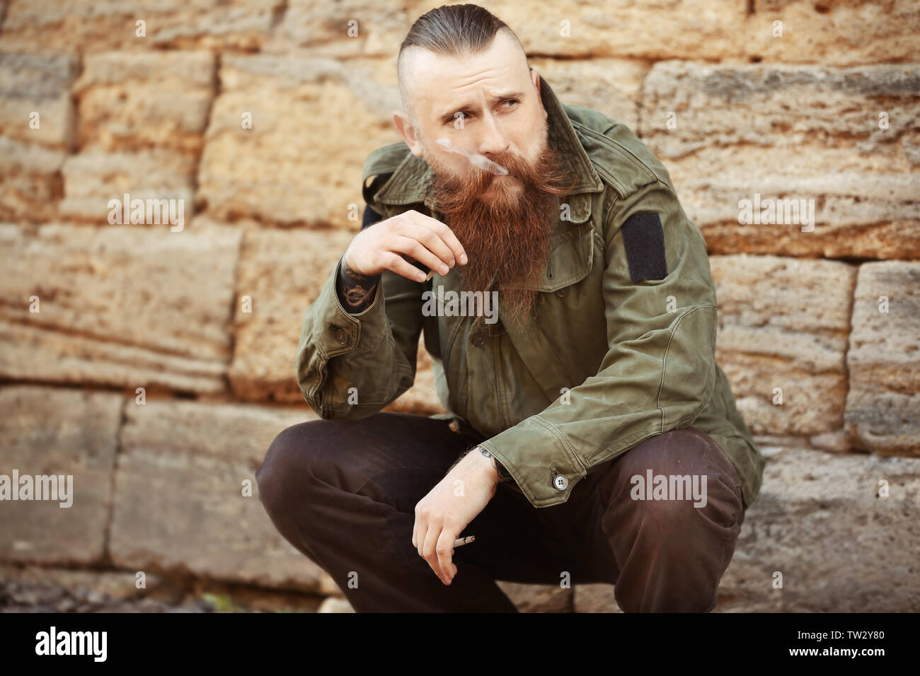 Homme barbu fumeurs à l'extérieur des mauvaises herbes Banque D'Images