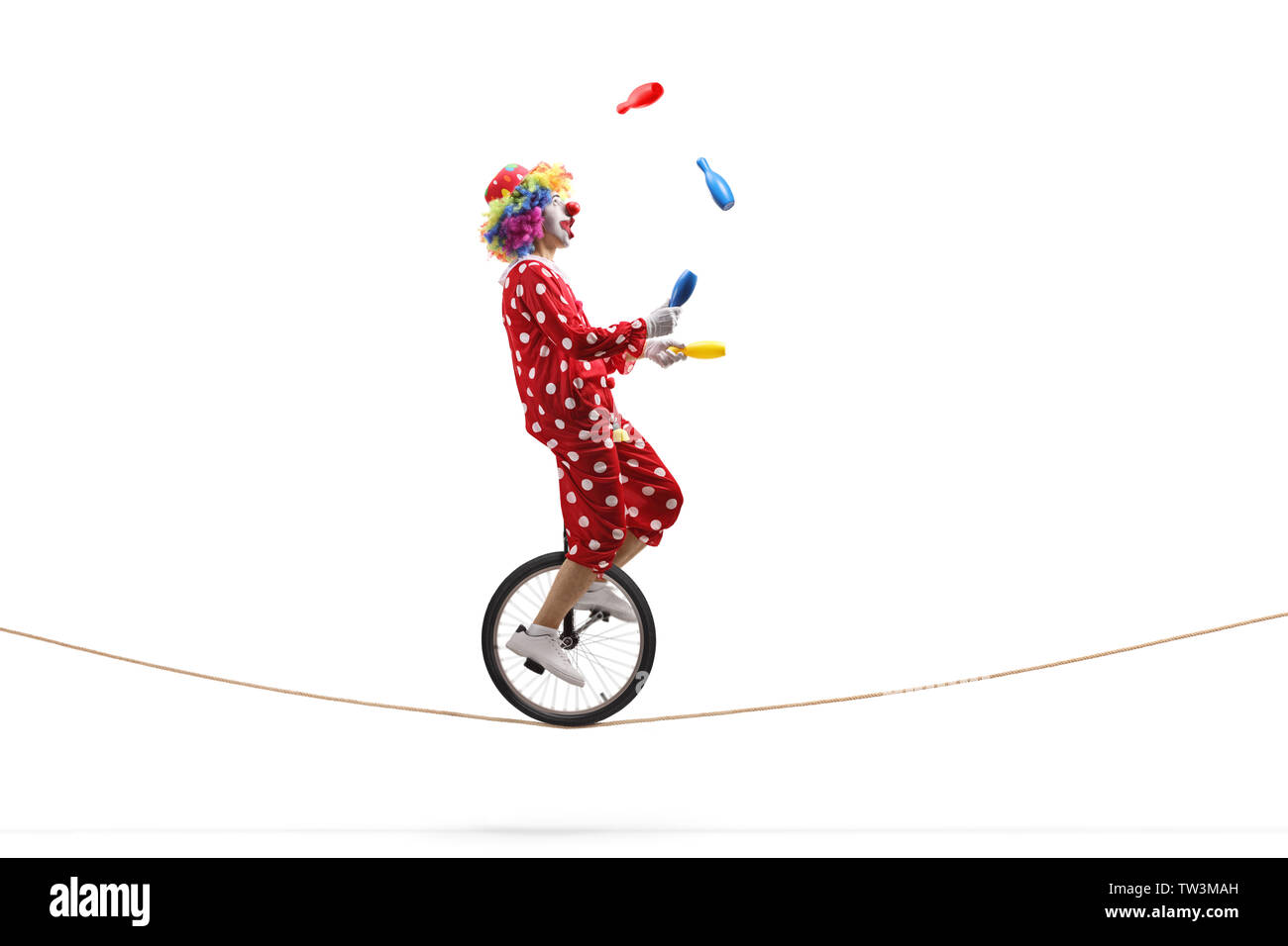 De toute la longueur d'un clown jonglant avec des clubs et de l'équitation un monocycle sur une corde isolé sur fond blanc Banque D'Images