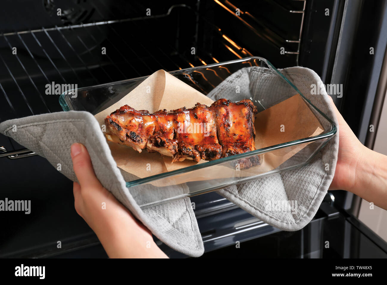 Jeune femme en tenant la plaque de cuisson avec des côtes de porc délicieux hors du four Banque D'Images