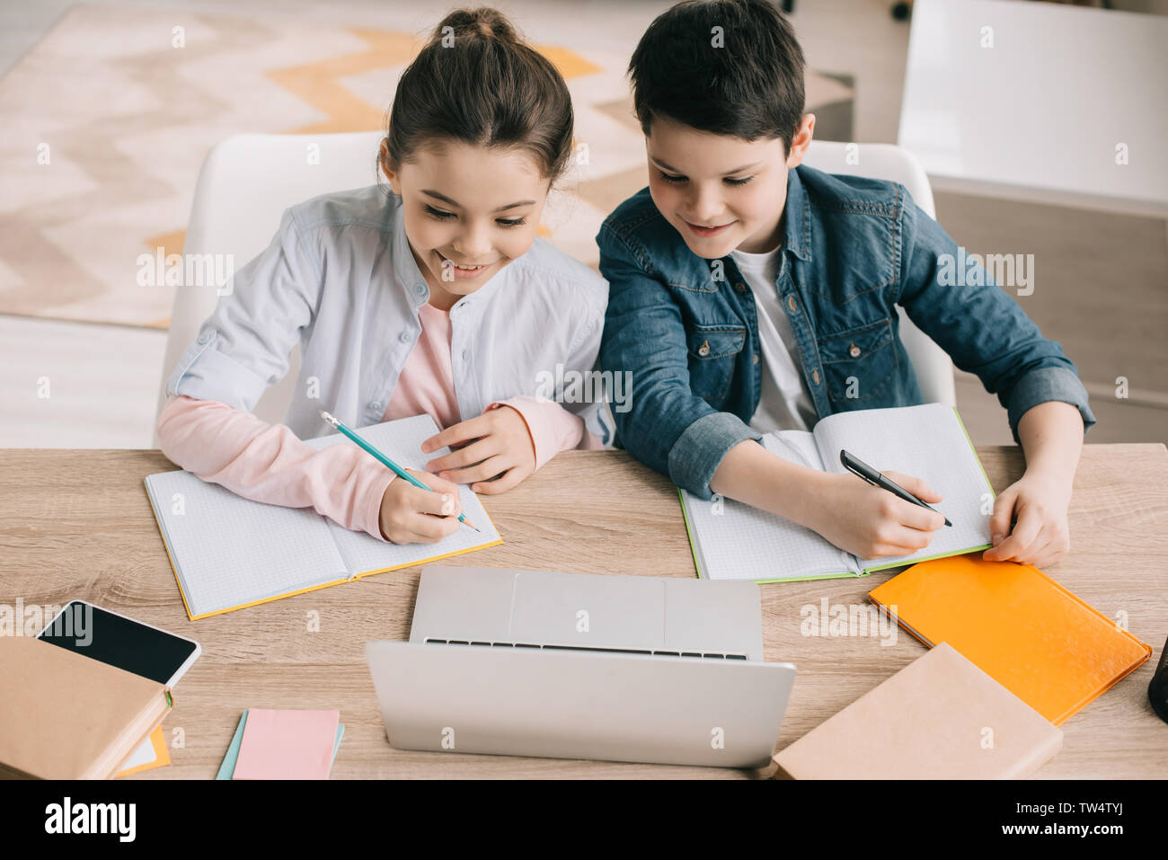 Smiling brother and sister écrit dans des carnets et using laptop together Banque D'Images